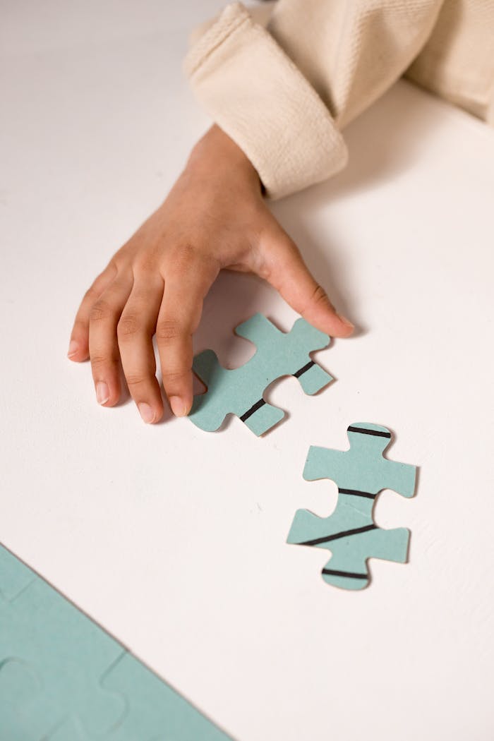 A child's hand in focus, solving a pastel blue puzzle, illustrating focus and learning.