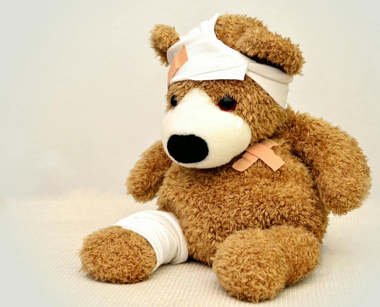A brown teddy bear with bandages, depicting a playful take on injury recovery in a minimalist setting.